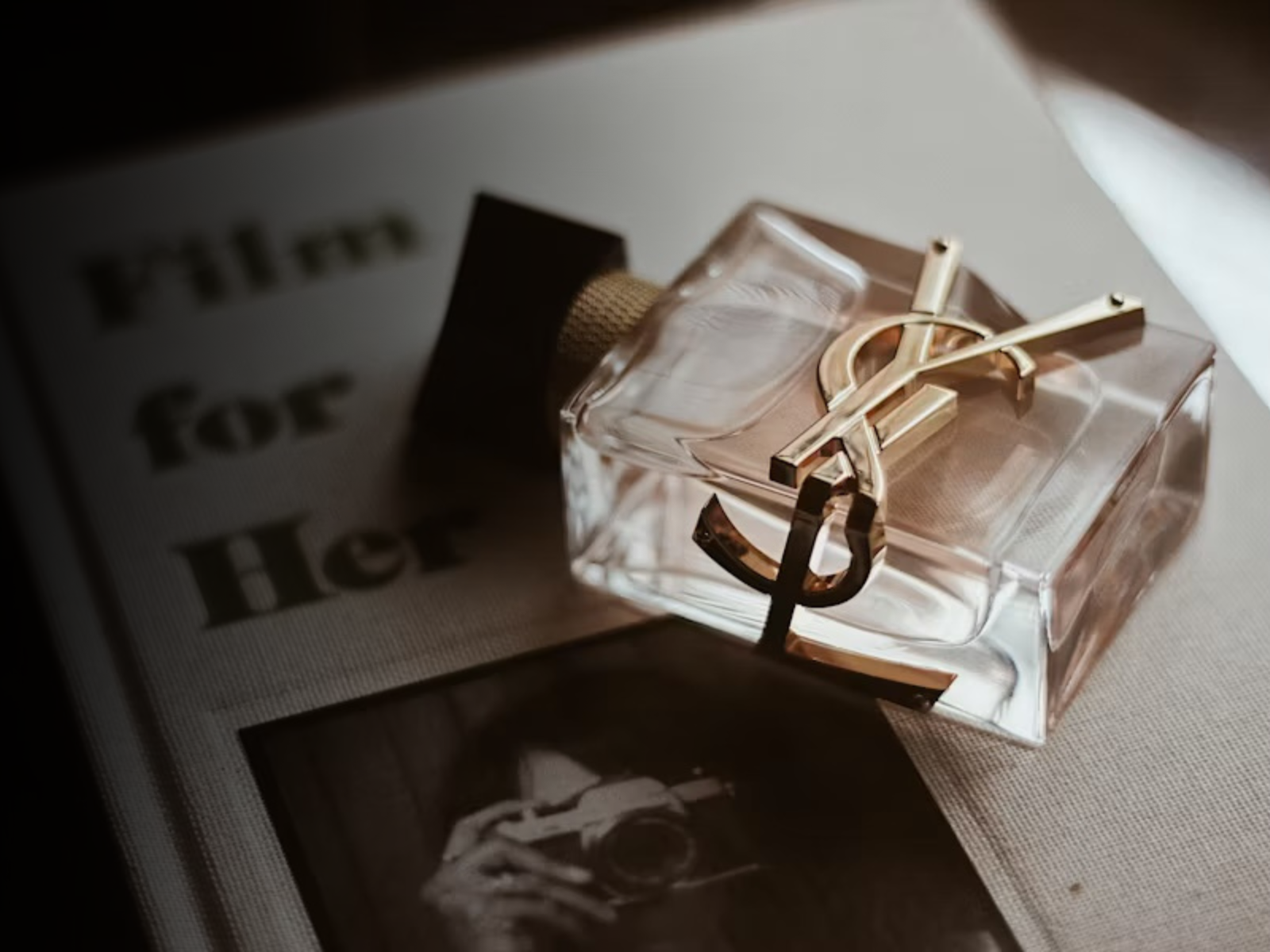 A crystal perfume bottle on antique books, beside a burning black candle, dried roses and handwritten notes on cream marble